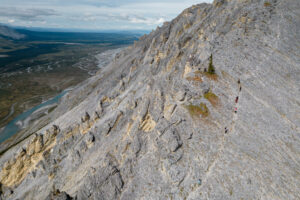 Aerial view of the group hiking up a large and rocky ridgeline, with clear views of surrounding valleys and mountains.