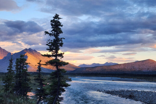 Landscape along the Wind River with diffuse sunlight that paints the clouds, sky, and mountains in orange and purple hues.