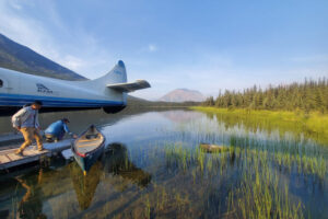 Participants board a floatplane parked near calm waters and surrounded by tall grasses and trees.