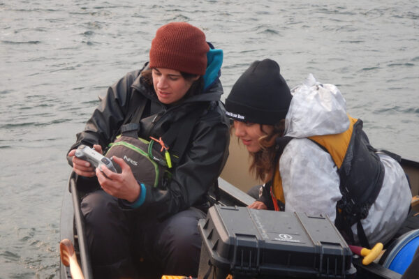 Bethany shows Shalaya how to use the drone while sitting inside a canoe.