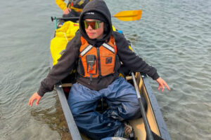 Chayce in the bow of a canoe smiles and reaches down to touch the water on either side.