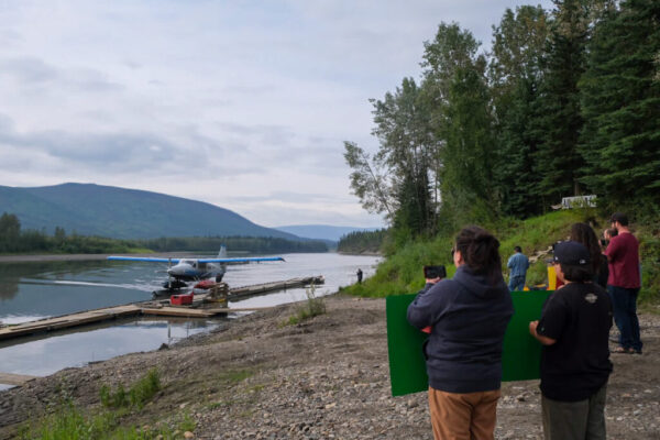 Community members stand on the riverbank and watch as the floatplane docks.