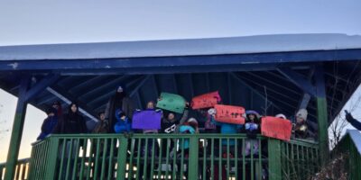 Group in Mayo, YT holds up colourful signs above their heads, some including children’s drawings, calling for protecting the Peel. First Nation of Na-Cho Nyäk Dun traditional territory, photo by Erin Holm.