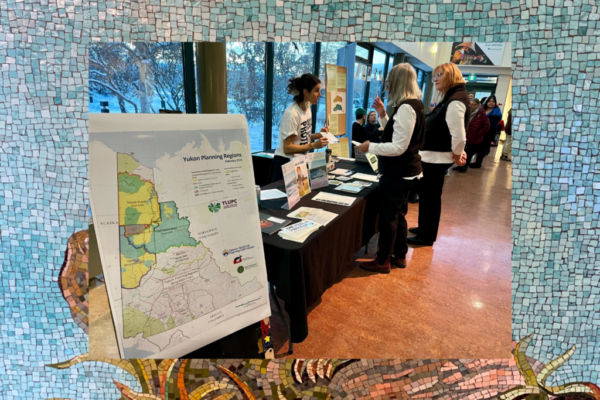 Map of Yukon Planning Regions sits in front of a table where our outreach manager (Joti) speaks to a few people about conservation while holding up a CPAWS flyer. Kwanlin Dün First Nation and the Ta’an Kwäch’än Council traditional territory, photo by Stephanie Woods.