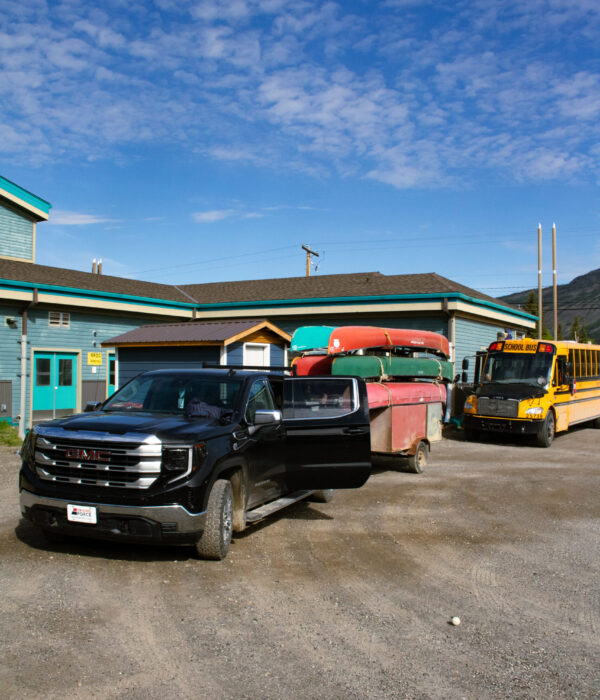 A black truck pulls multiple canoes in front of the Ross River school. Photo by Hannah Hofsink, Ross River Dena Council territory.